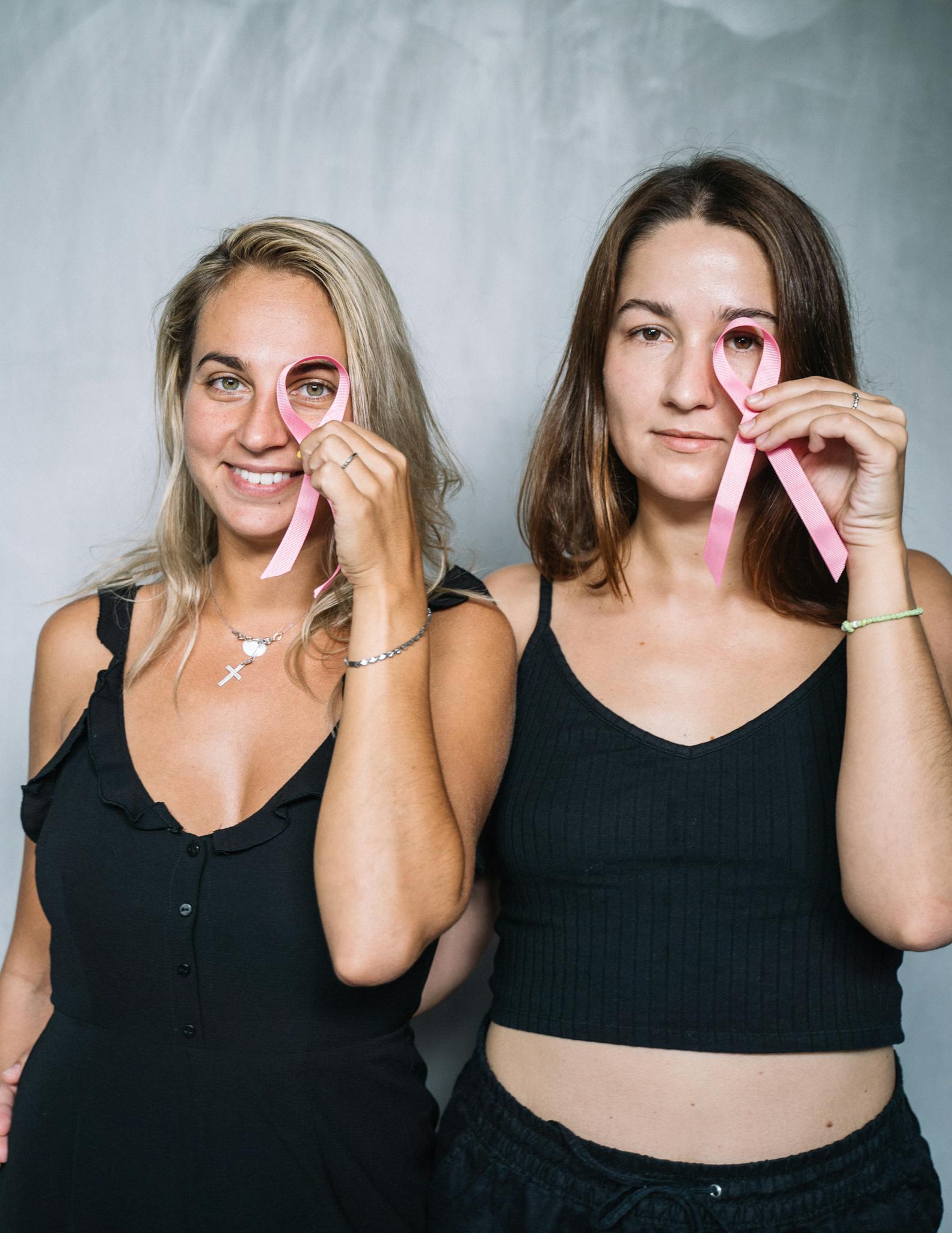 Two women holding pink ribbons for breast cancer awareness, promoting health.